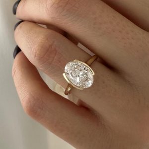East-west oval diamond engagement ring with partial bezel setting on a tapered polished band