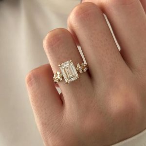 Emerald cut engagement ring with four prongs, split shank, and floral pavé accents