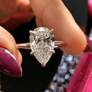 Pear solitaire engagement ring with accent stones in basket setting on slim polished band
