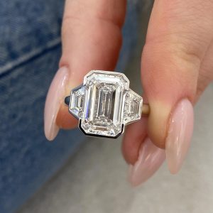 Bezel set emerald cut engagement ring with trapezoid side stones on a polished band